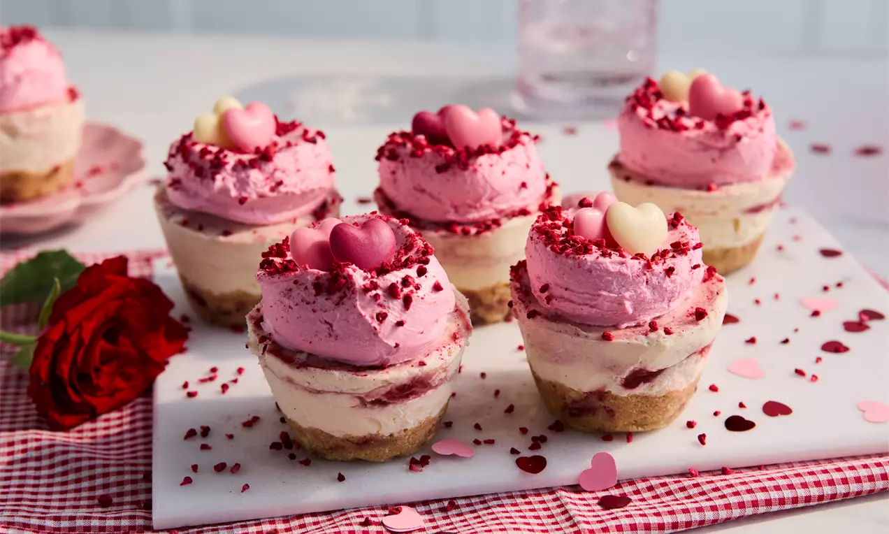 Mini cheesecakes with biscuit bases, swirled cream layers, topped with pink raspberry mousse, candy hearts and raspberry crumble