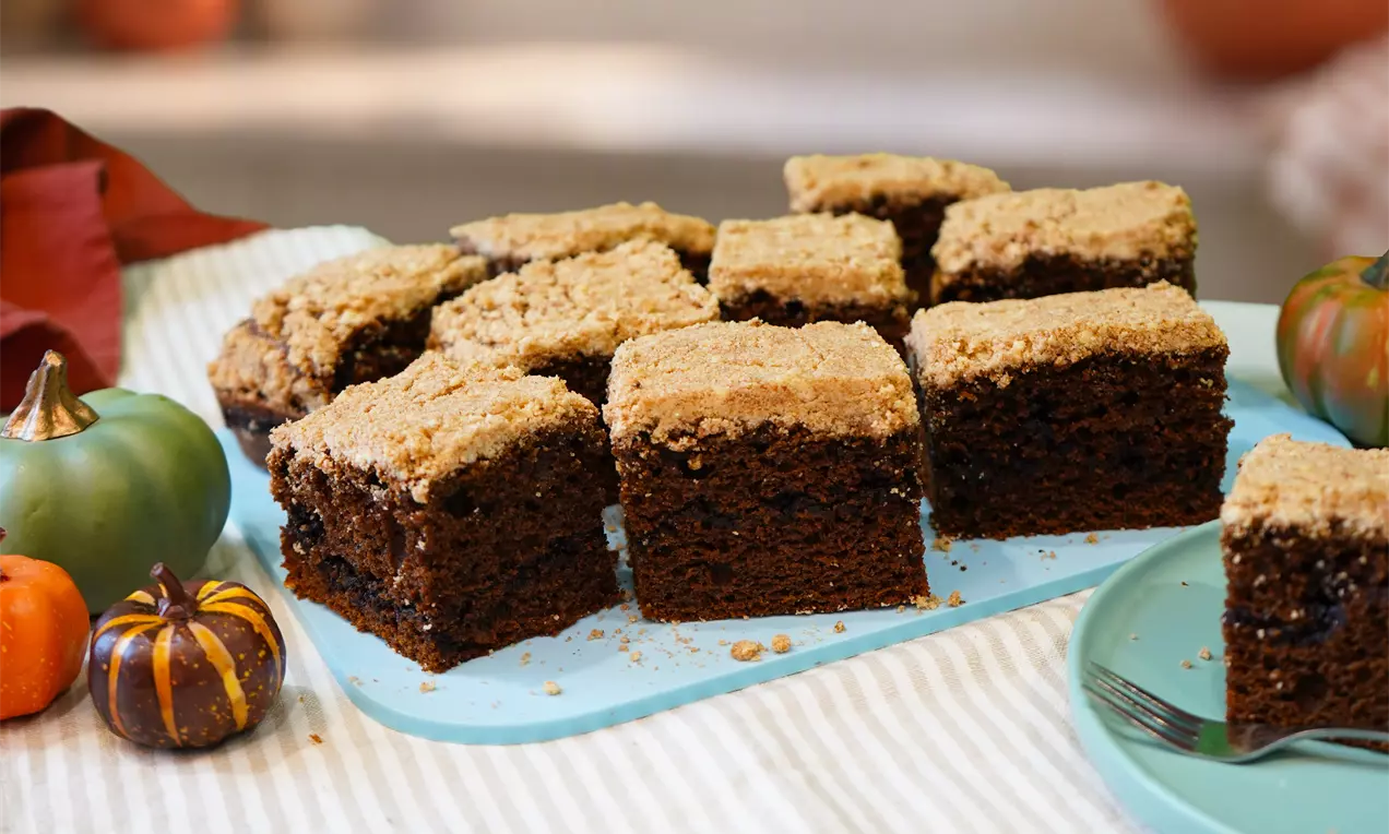 Square slices of rich brown pumpkin spiced coffee cake topped with golden crumbly streusel on a light blue tray with mini pumpkins, AI-labeled image