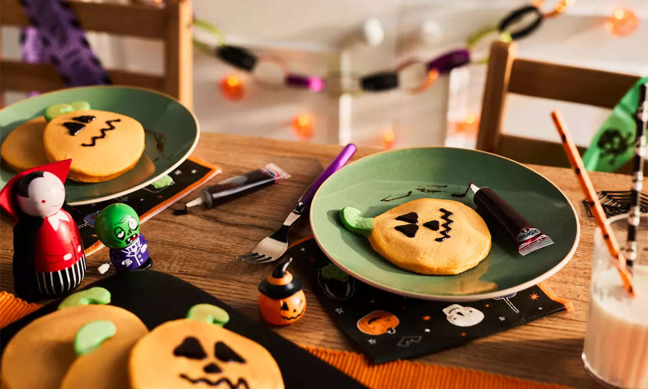 Golden round pancakes shaped like pumpkins with green candy stems and black icing jack-o'-lantern faces on green plates