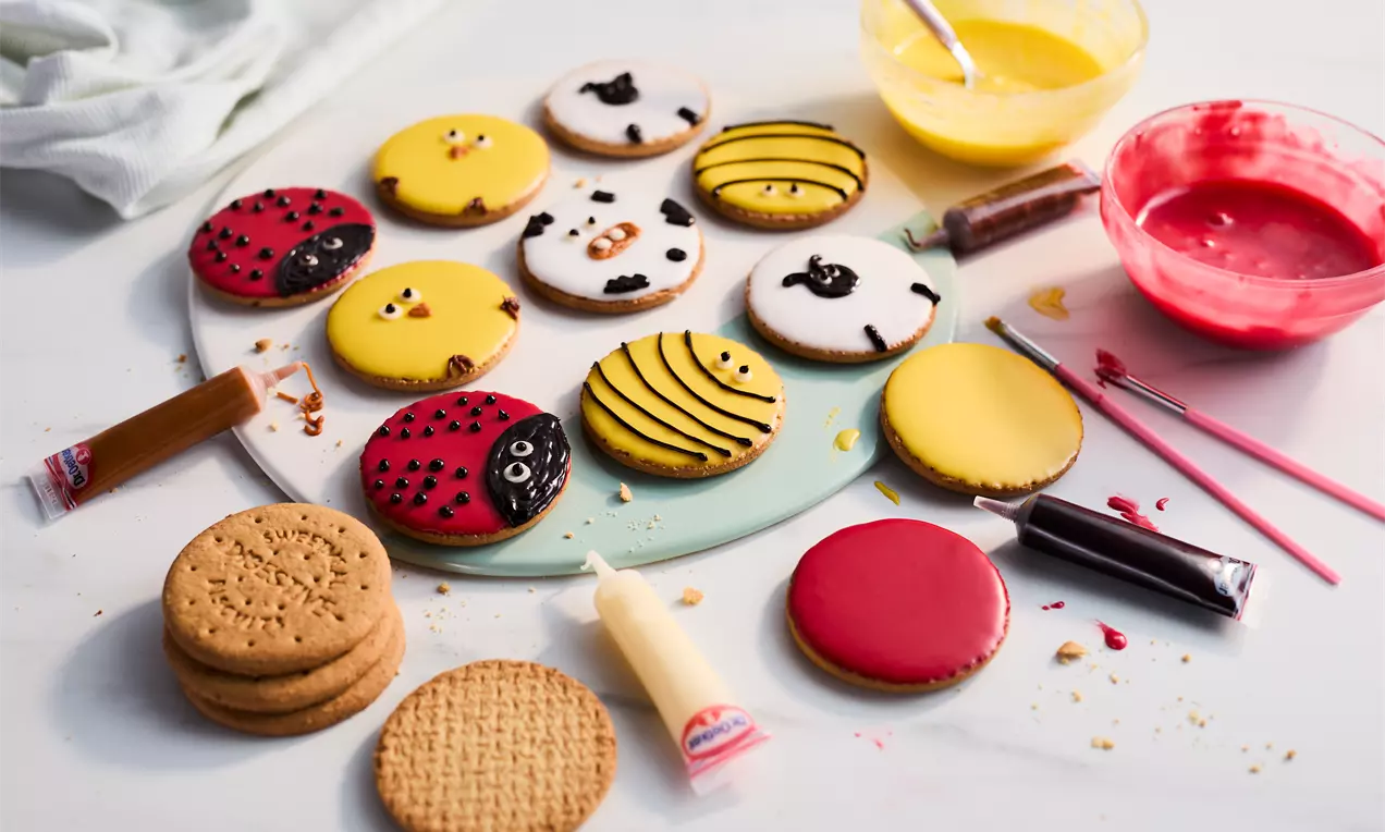 Round biscuits with colourful animal designs, like red ladybugs, yellow bees, and white sheep, arranged on a pastel green plate