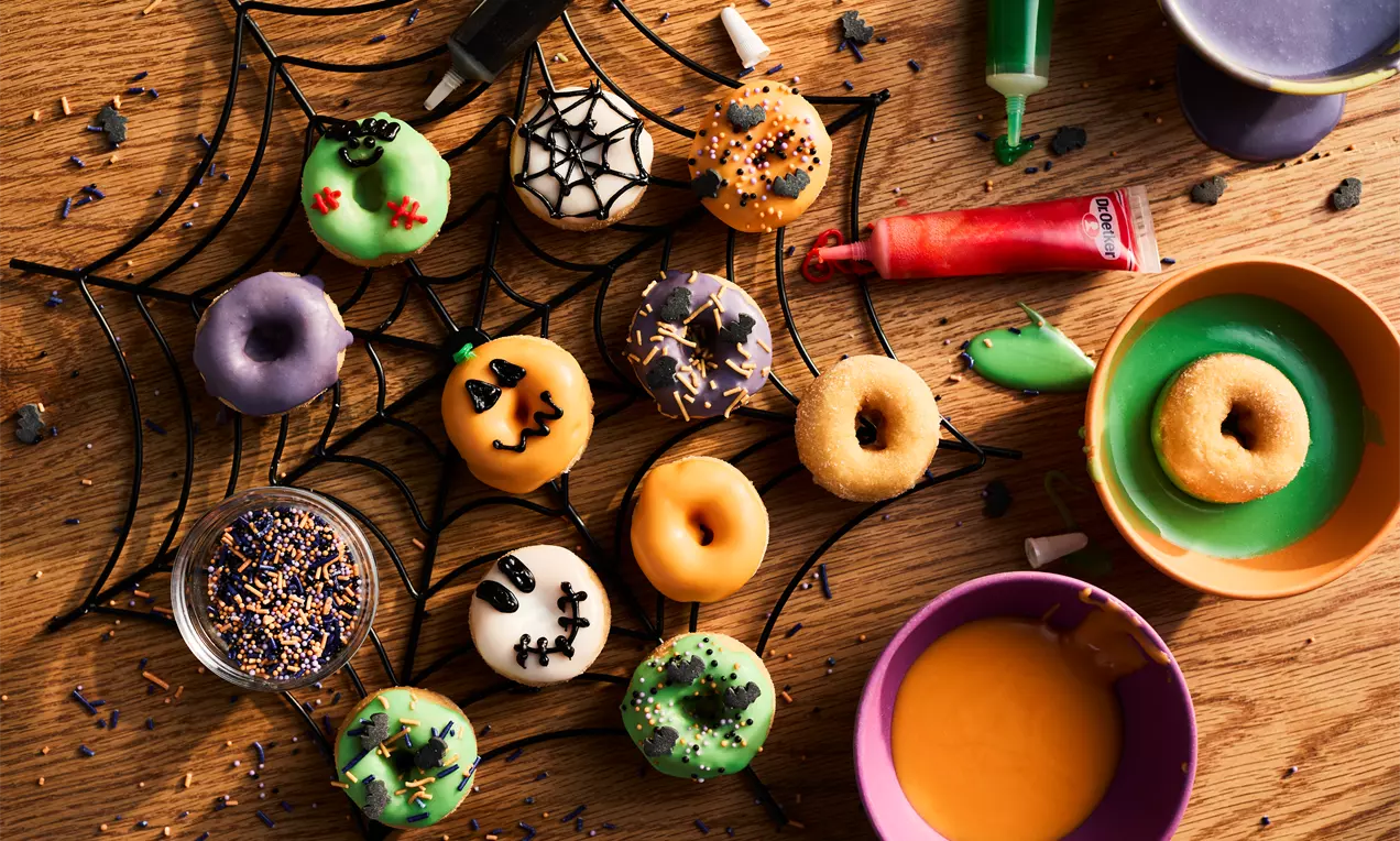 Colourful Halloween doughnuts in green, orange, white, and purple icing with spooky decorations arranged on a black spiderweb tray