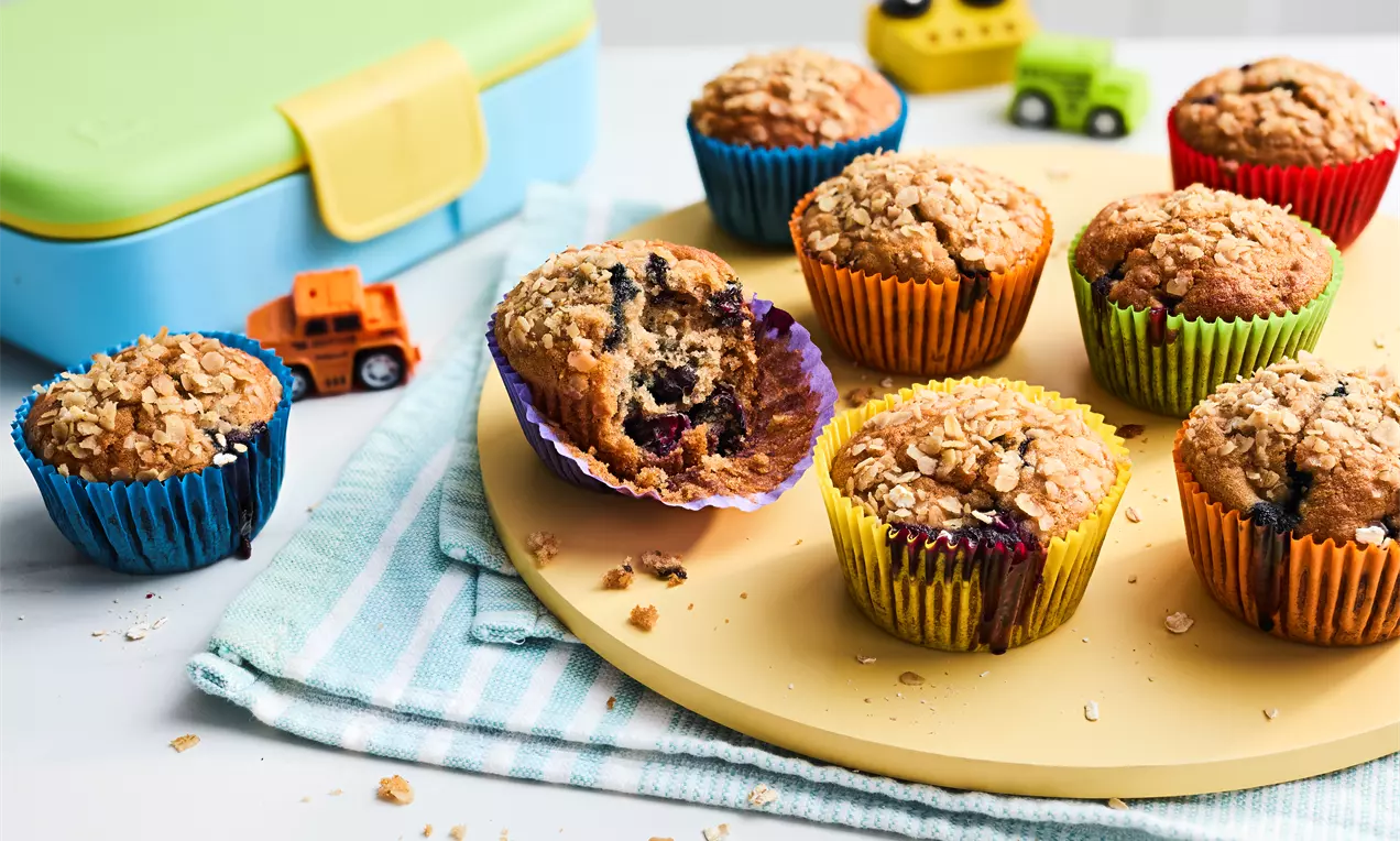 Golden-brown breakfast muffins with crumbly tops and colourful paper wrappers, arranged on a round yellow tray with toy cars nearby