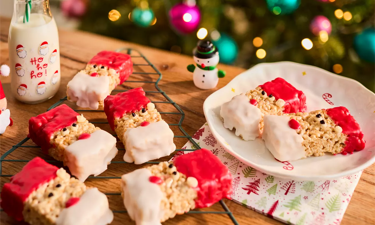 Rice Krispies square treats decorated as Santa faces with red candy hats, white icing beards, and black and red candy details on a festive table