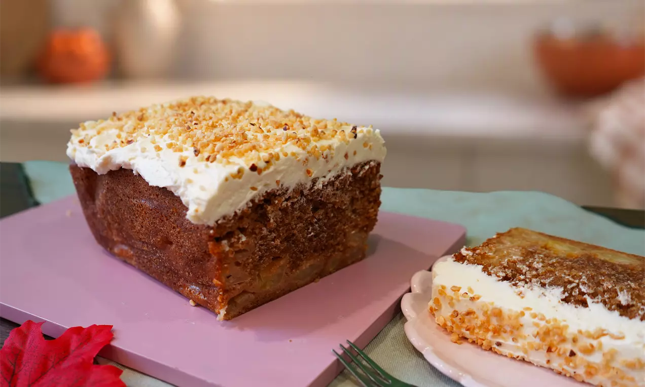 Caramelised apple cake with a golden-brown moist base, creamy white topping sprinkled with crunchy crumbs, served on pastel plates, AI-labeled image